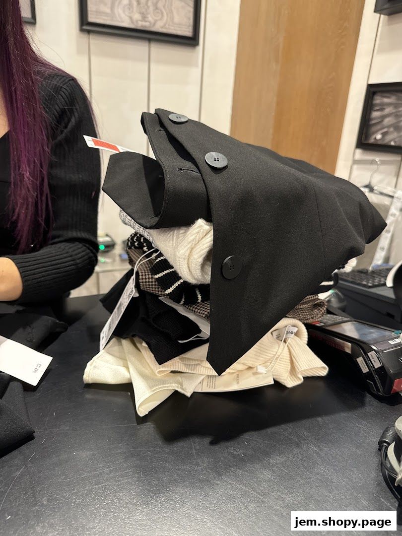 A stack of folded clothing items, including a black blazer, on a counter at a MANGO store.