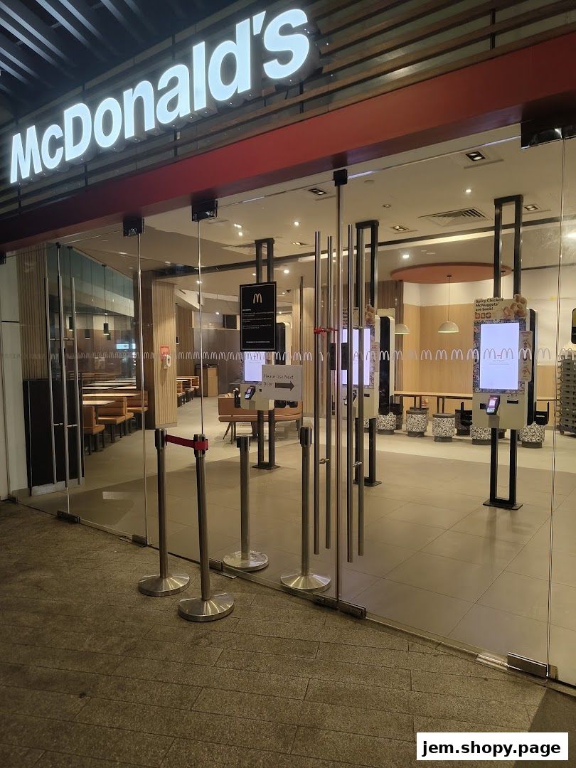The entrance of a McDonald's restaurant with digital ordering kiosks and seating visible inside.