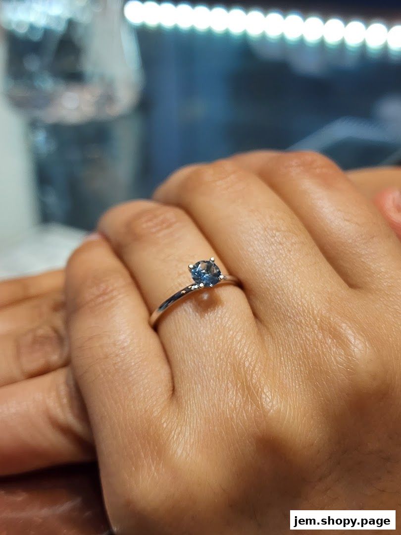 A close-up shot of a hand wearing a delicate silver ring with a blue gemstone.