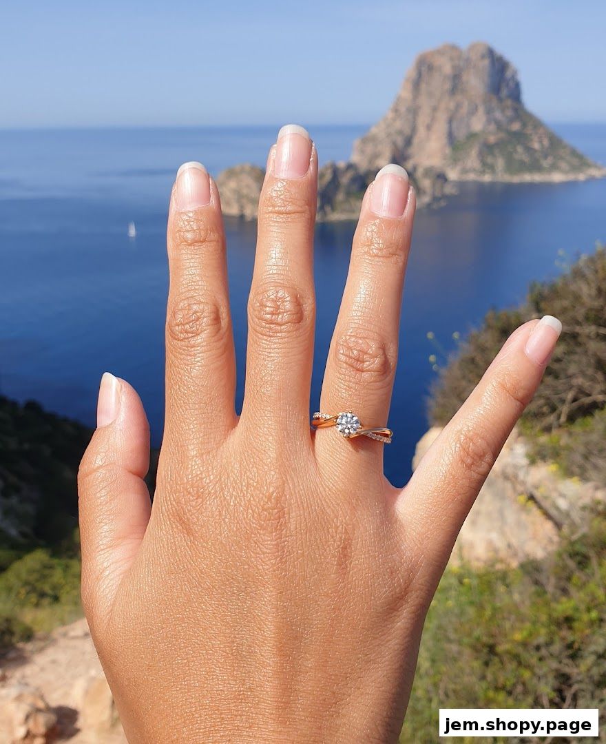 A hand wearing a diamond ring with a scenic ocean and island backdrop.