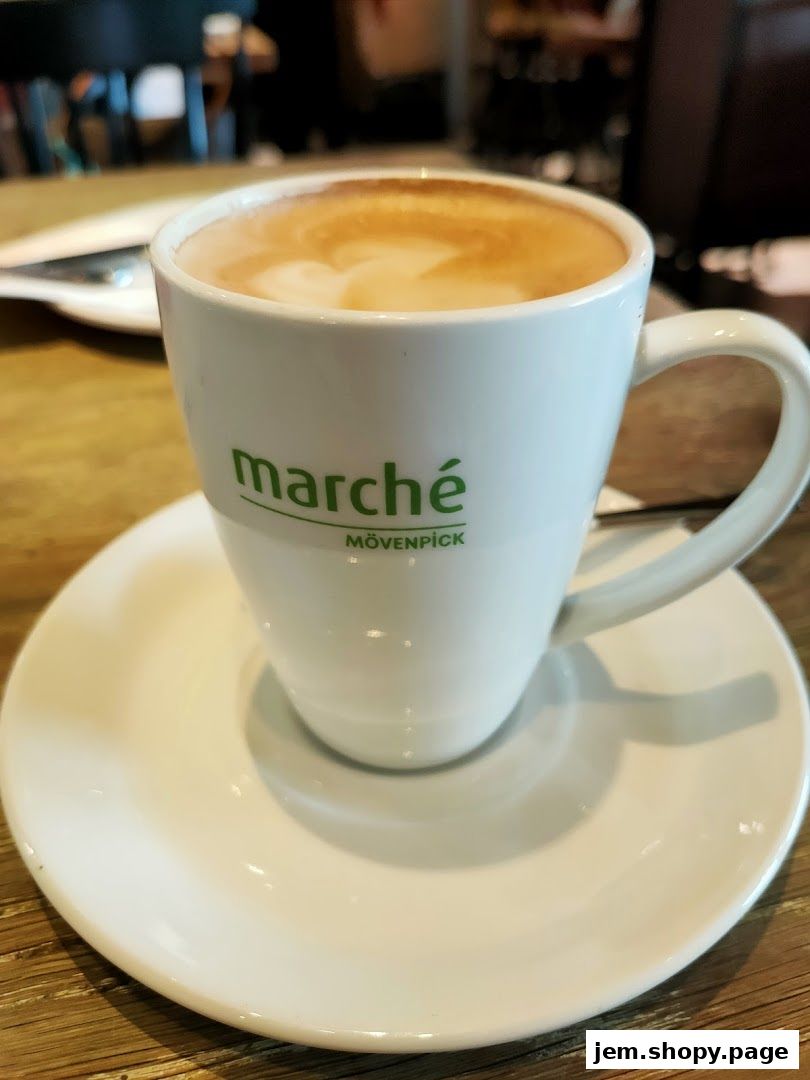 A close-up of a latte with latte art in a white mug with the Marche Movenpick logo.