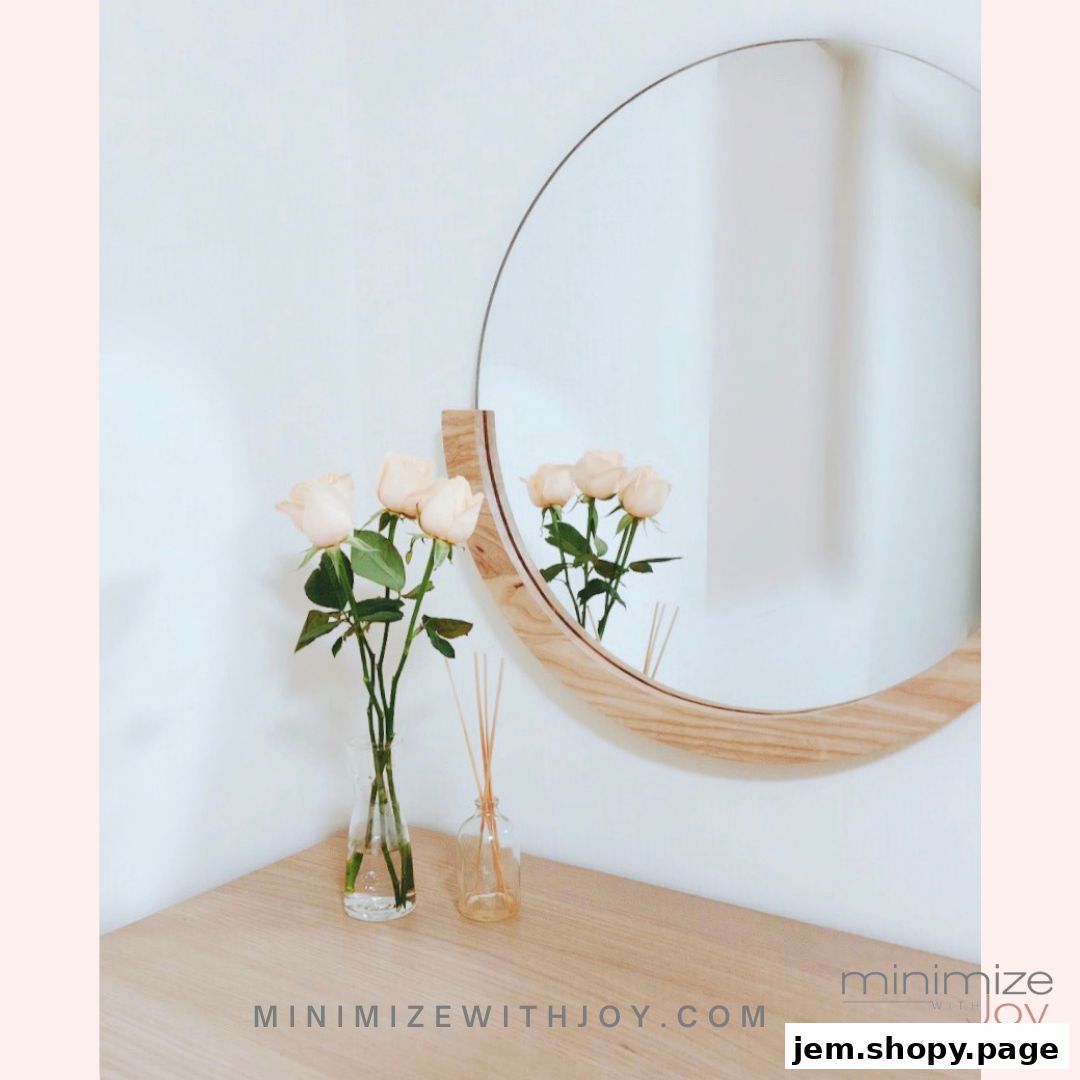 A minimalist display with roses in a vase and a diffuser next to a round mirror.