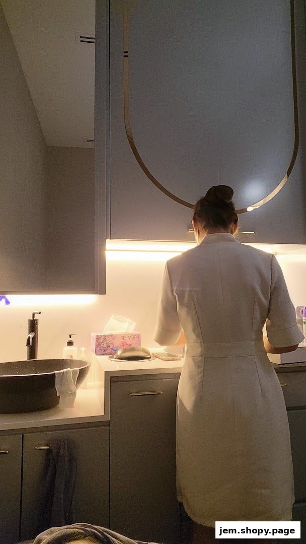 Aesthetician in uniform preparing a treatment area with sink and supplies.