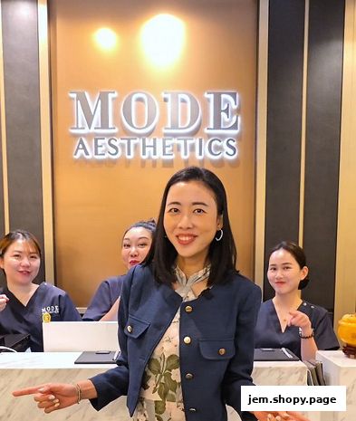 A woman in a blue jacket stands in front of the MODE Aesthetics reception with staff behind her.