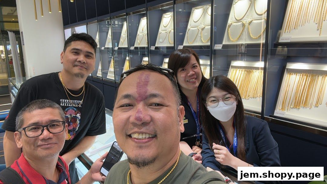 A group of people smiling in front of a display of gold necklaces at a pawnshop.