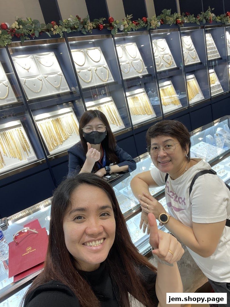Three smiling people pose in front of display cases filled with gold jewelry at MoneyMax Pawnshop.