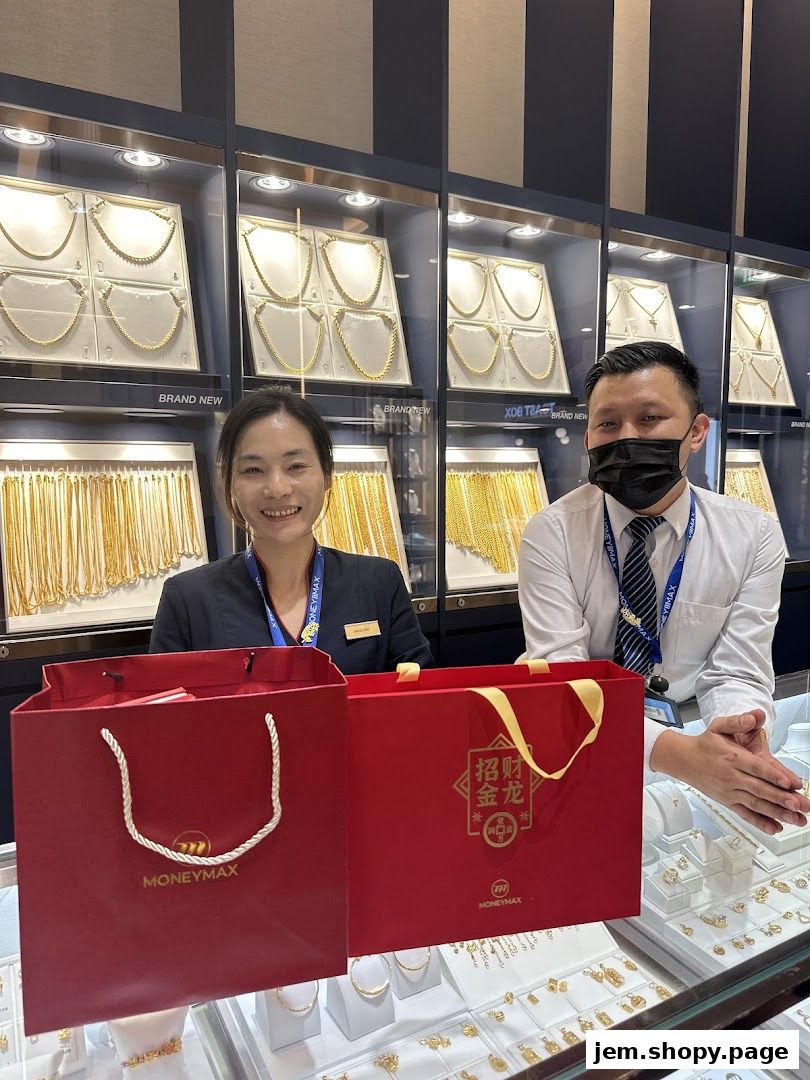 Two staff members stand behind a counter displaying gold jewelry and branded shopping bags.