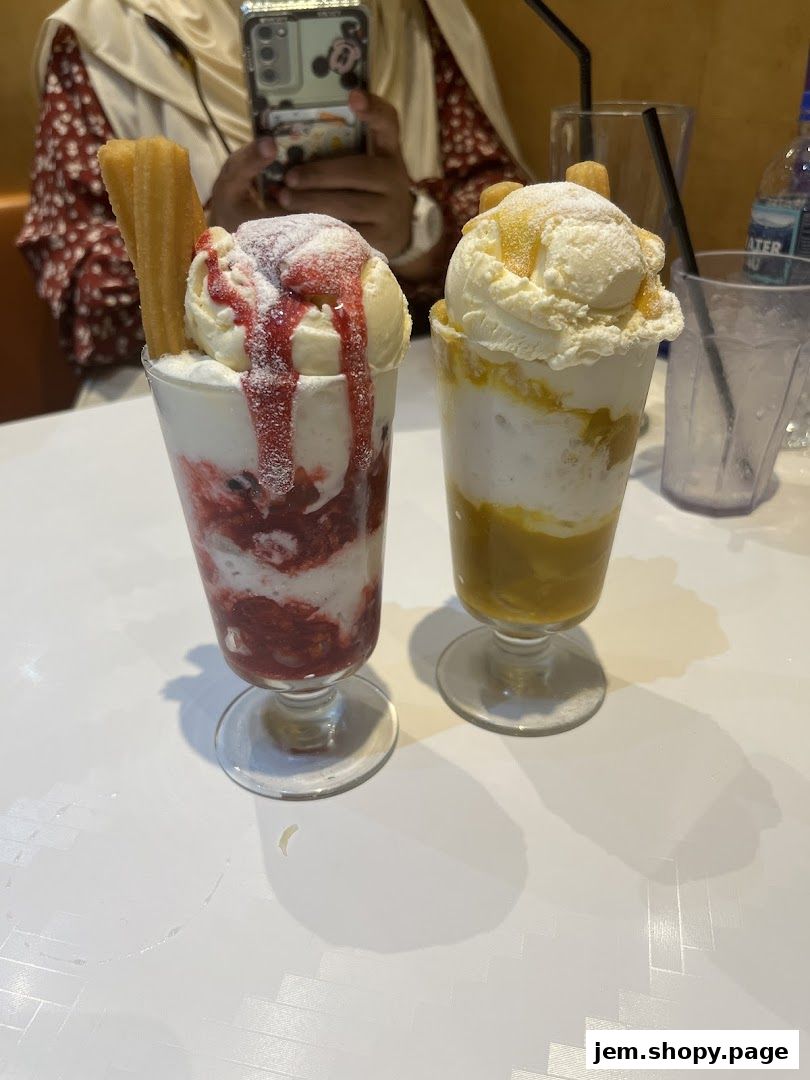 Two delicious ice cream sundaes with toppings and churros on a white table.