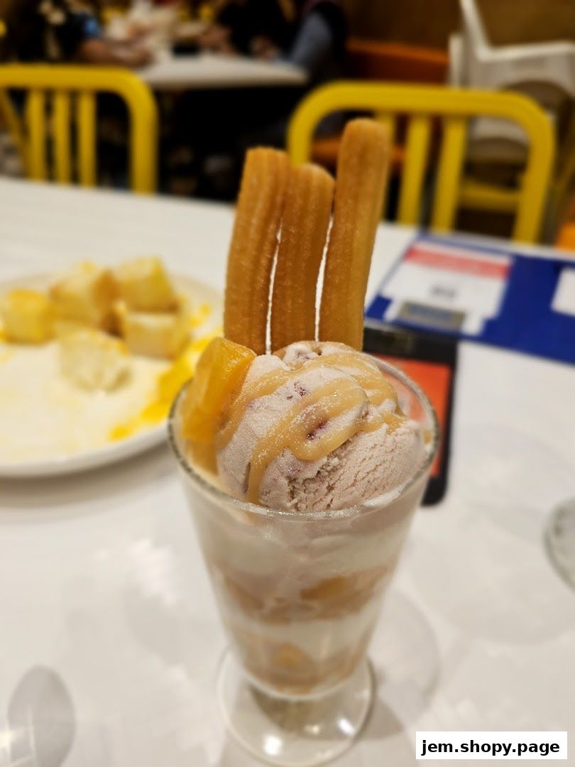 A tall glass filled with ice cream, fruit, and churros, served at a table.