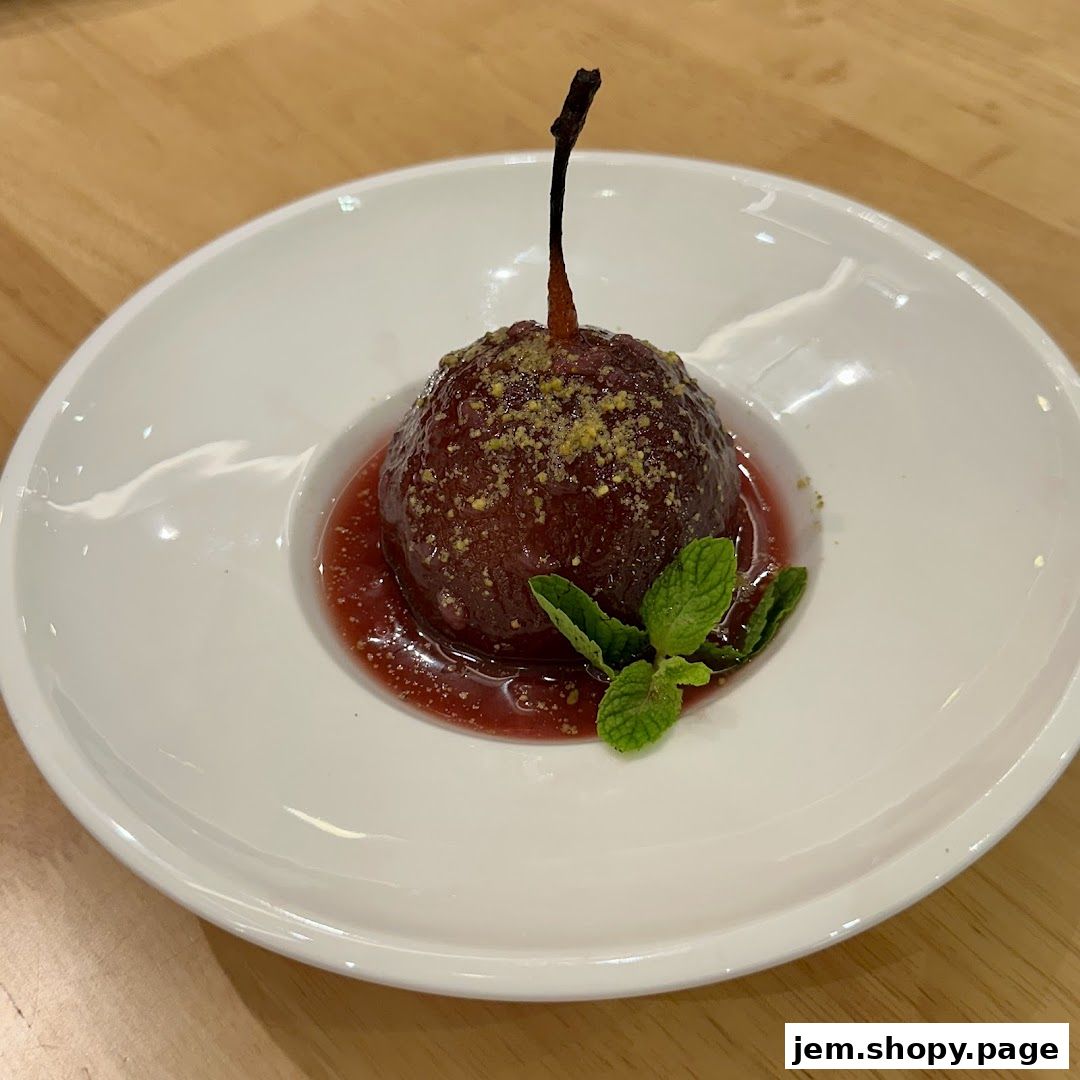 A beautifully presented poached pear dessert with berry sauce and mint garnish.