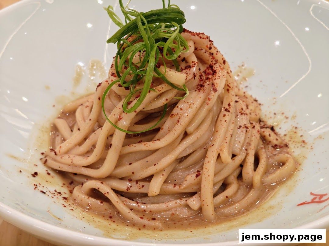 A close-up of a bowl of noodles topped with green onions and chili flakes.