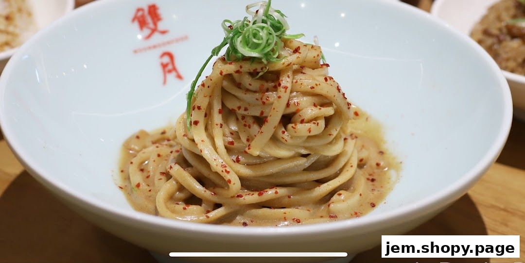 A close-up of a bowl of noodles with sauce and chili flakes, garnished with green onions.