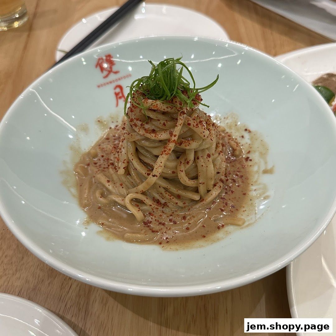 A close-up of a bowl of noodles with sauce and chili flakes, garnished with green onions.