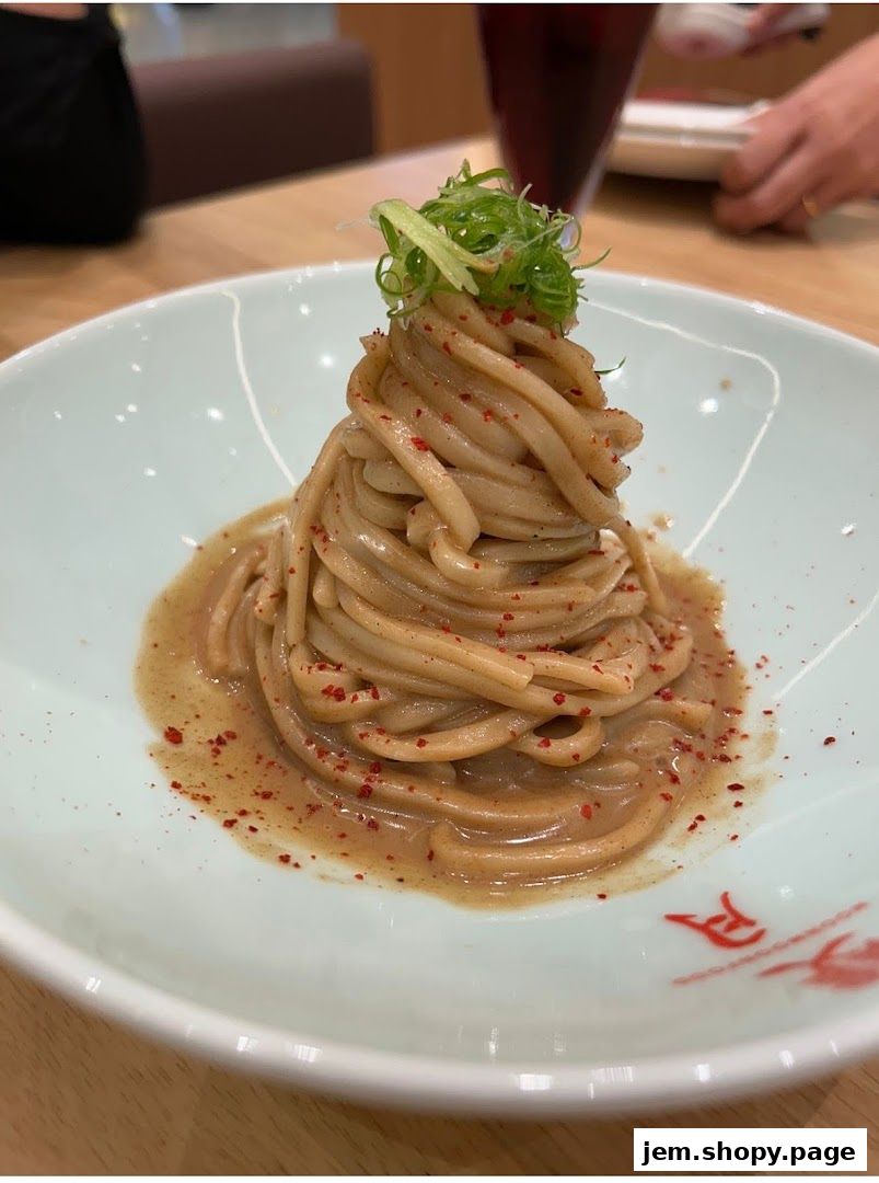A meticulously plated bowl of noodles with a savory sauce and a garnish of green onions.