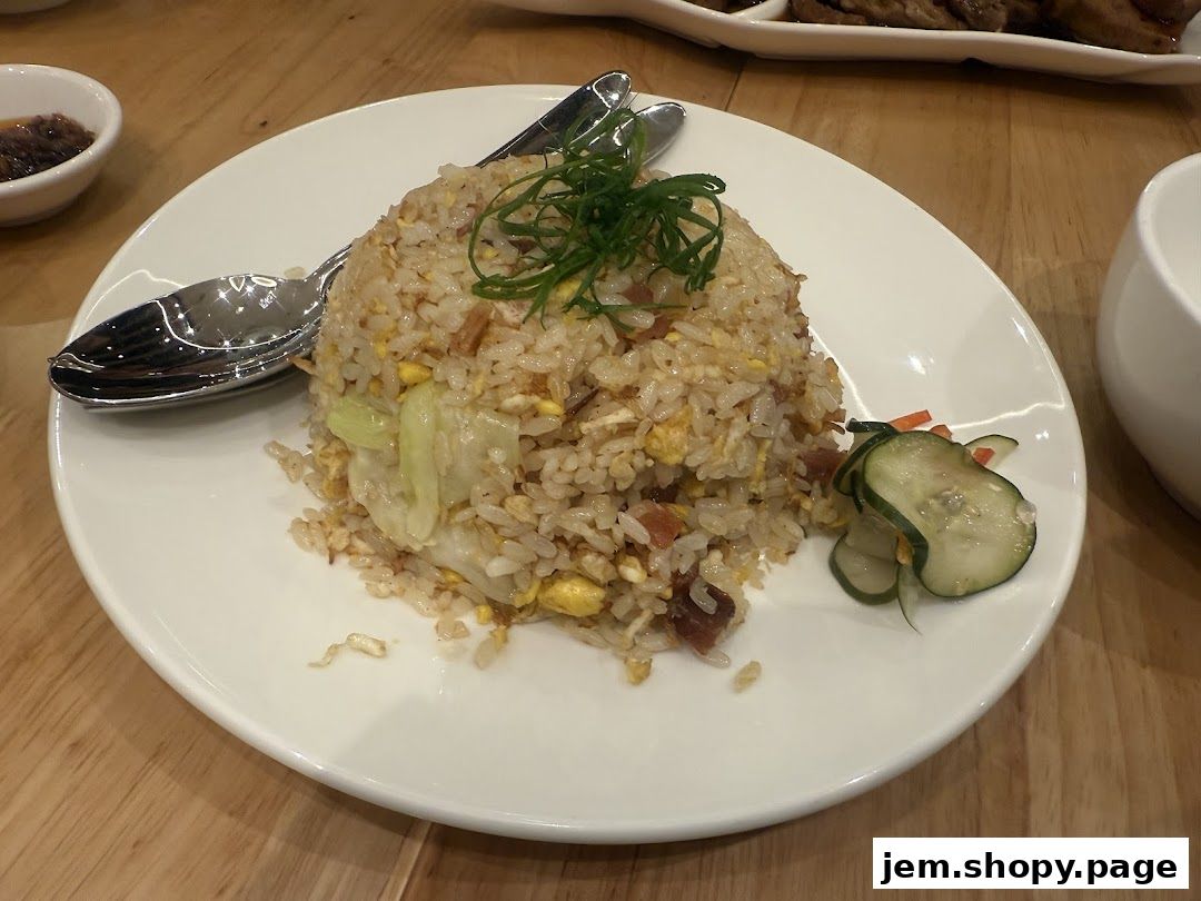 A plate of fried rice with garnishes and a side of pickles on a wooden table.