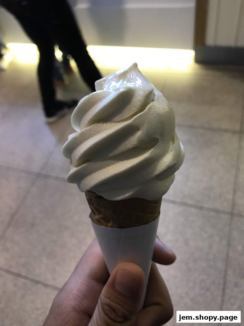 A hand holds a soft-serve ice cream cone with a waffle cone.