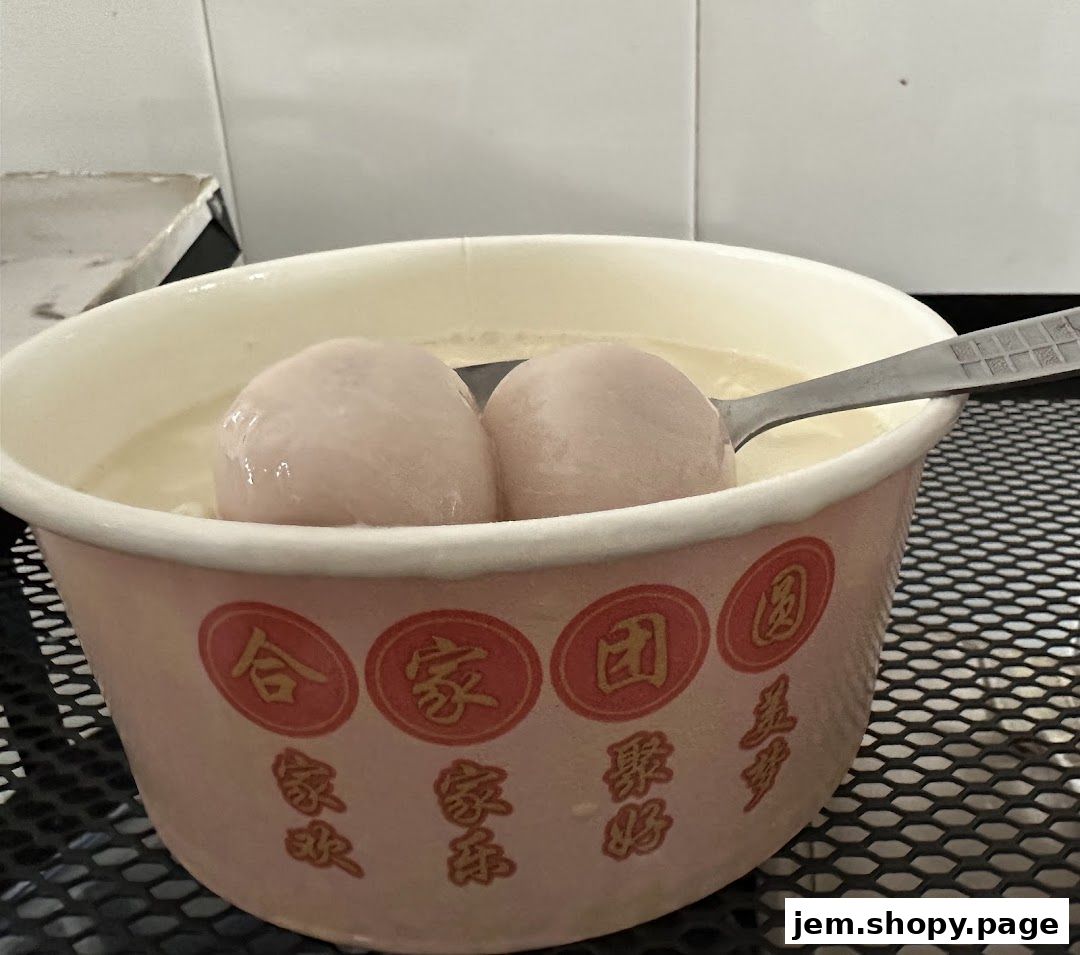 A bowl of sweet soup with two large dumplings and a spoon.