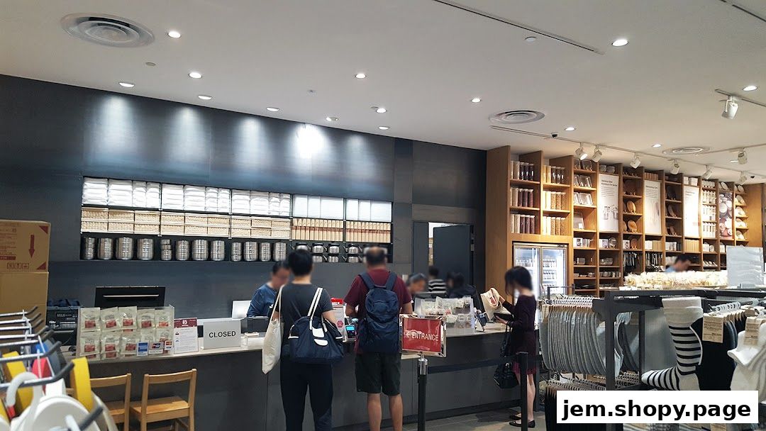 Customers at the checkout counter of a MUJI store with shelves of products in the background.