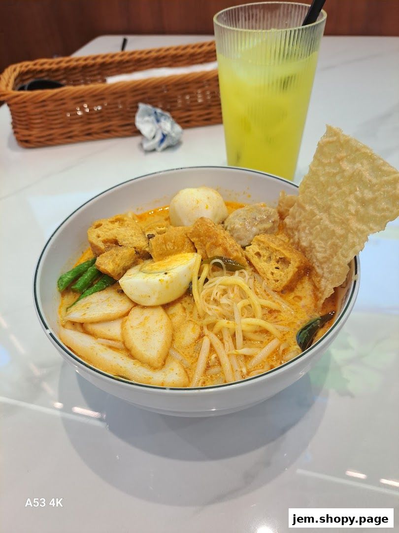 A bowl of delicious curry laksa with a refreshing drink on the side.