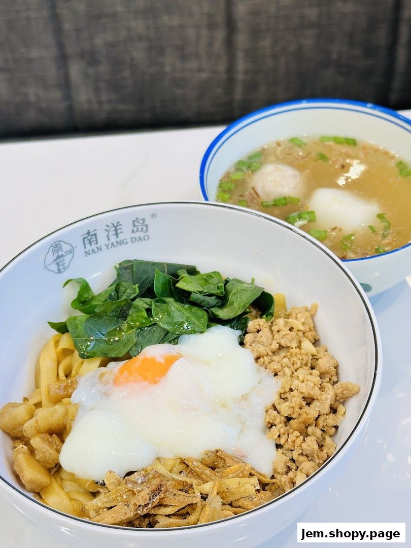 A bowl of noodles with egg, minced meat, vegetables, and a side of soup.