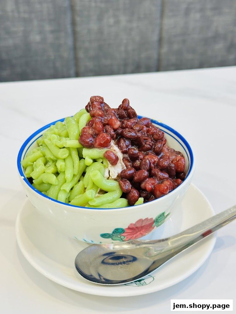 A refreshing bowl of Cendol with red beans and shaved ice, served with a spoon.