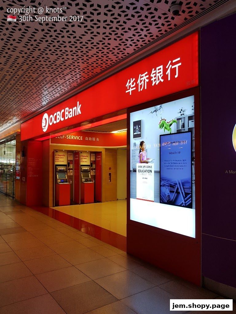 The exterior of an OCBC Bank branch with self-service machines and digital displays.