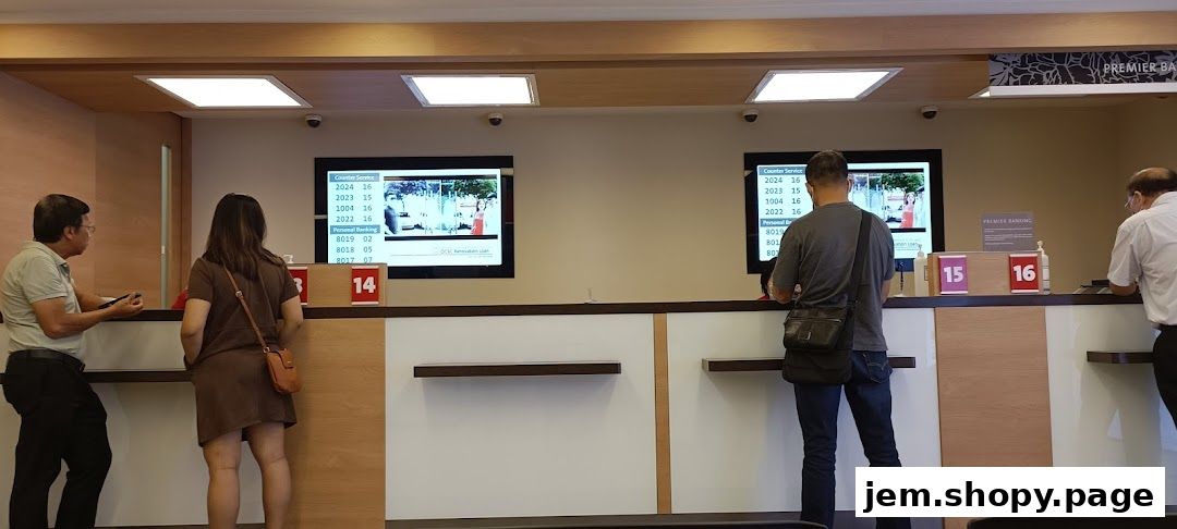 Customers wait at counters in a bank with digital displays showing queue numbers.