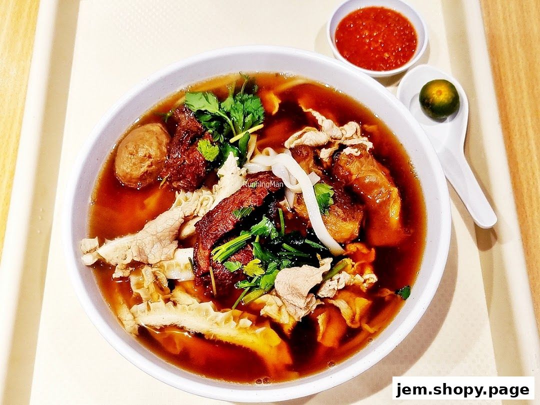 A bowl of beef noodles with various cuts of beef, tripe, and meatballs, served with chili sauce and lime.