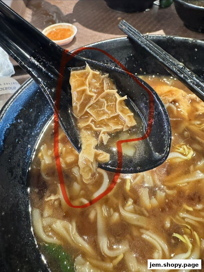 A close-up of a bowl of beef noodles with tripe highlighted on a spoon.
