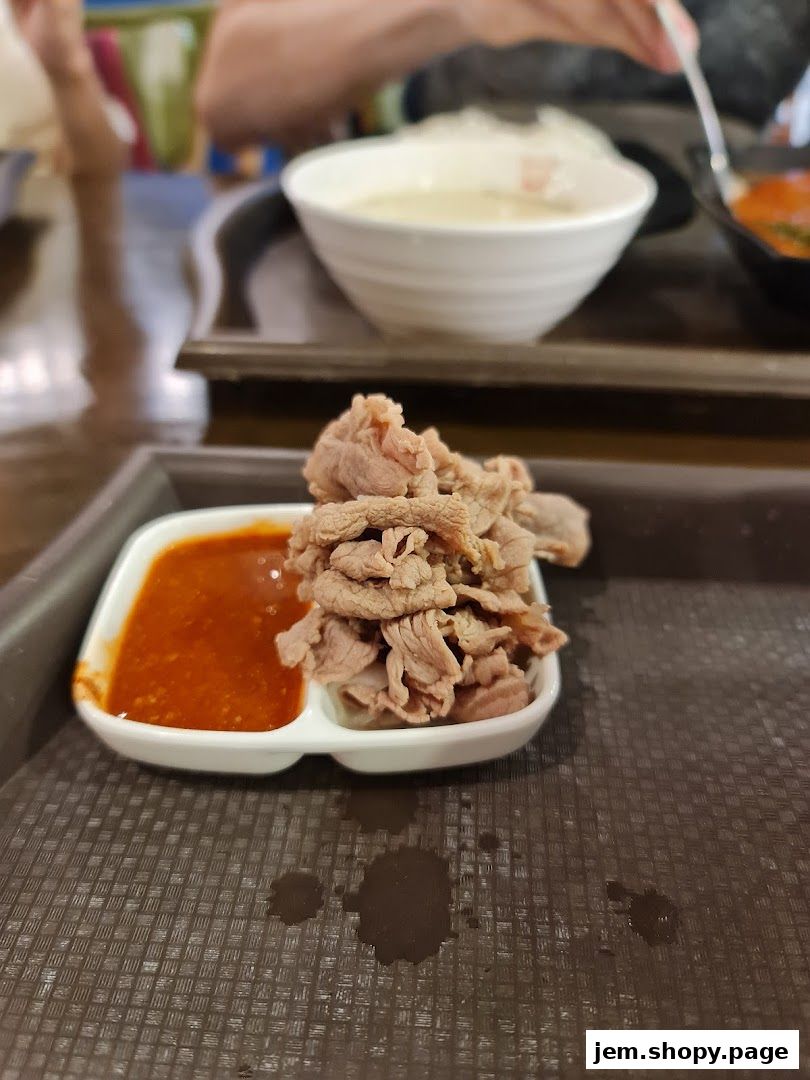 A close-up of thinly sliced beef with dipping sauce, served at Odeon Beef Noodles.