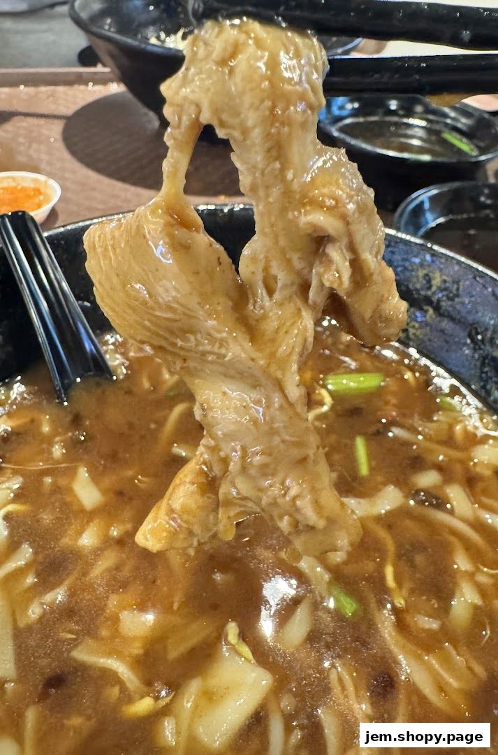 Close-up of tender beef noodles in a rich broth, with chopsticks holding a piece of beef.