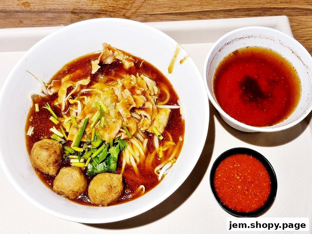 A bowl of beef noodles with meatballs, broth, and a side of chili sauce.