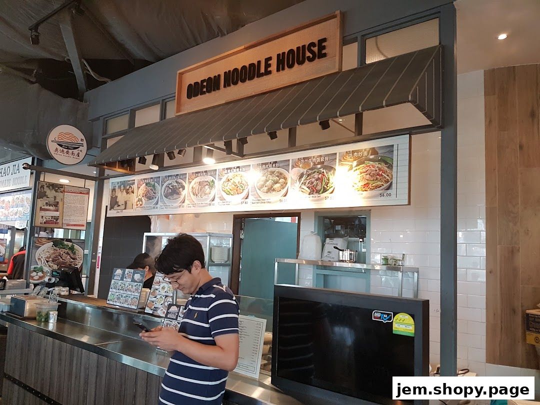 Odeon Noodle House storefront with a menu display and a customer looking at their phone.