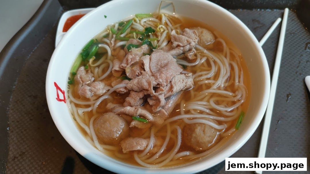 A close-up shot of a steaming bowl of beef noodles with meatballs and bean sprouts.