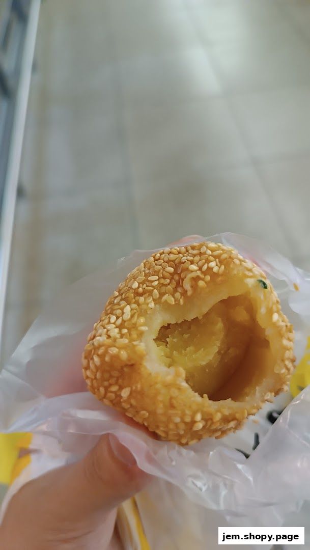 A hand holds a sesame-seed coated pastry with a bite taken out, revealing a sweet filling.