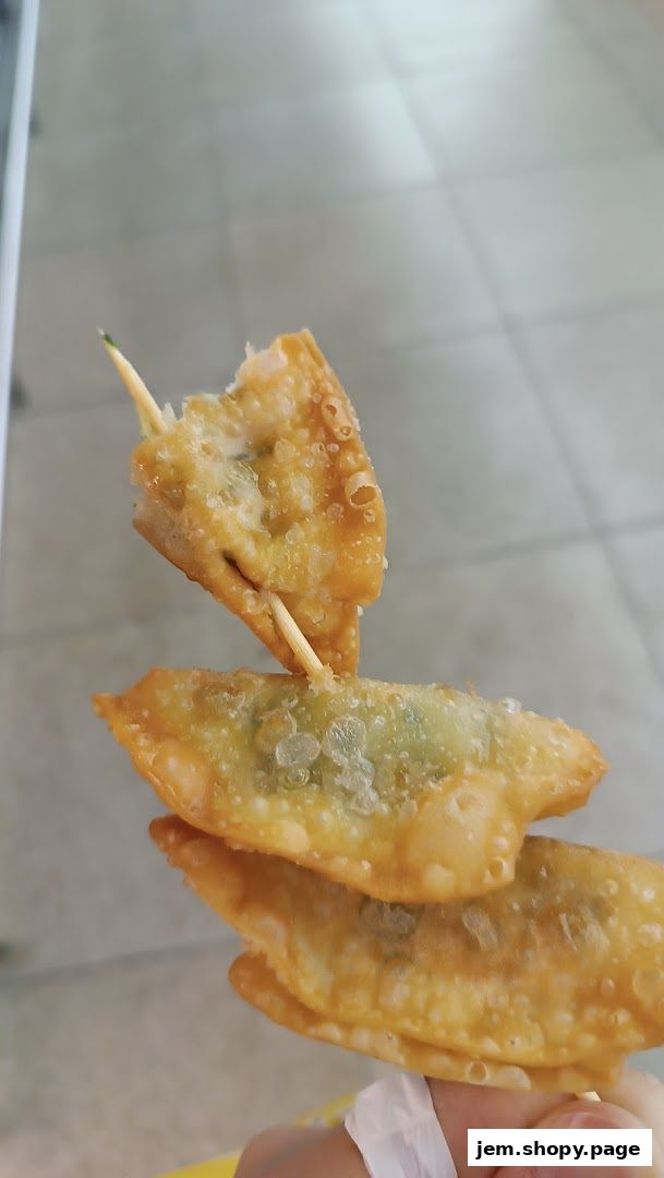 Close-up of three crispy fried dumplings on a skewer, with one bitten.