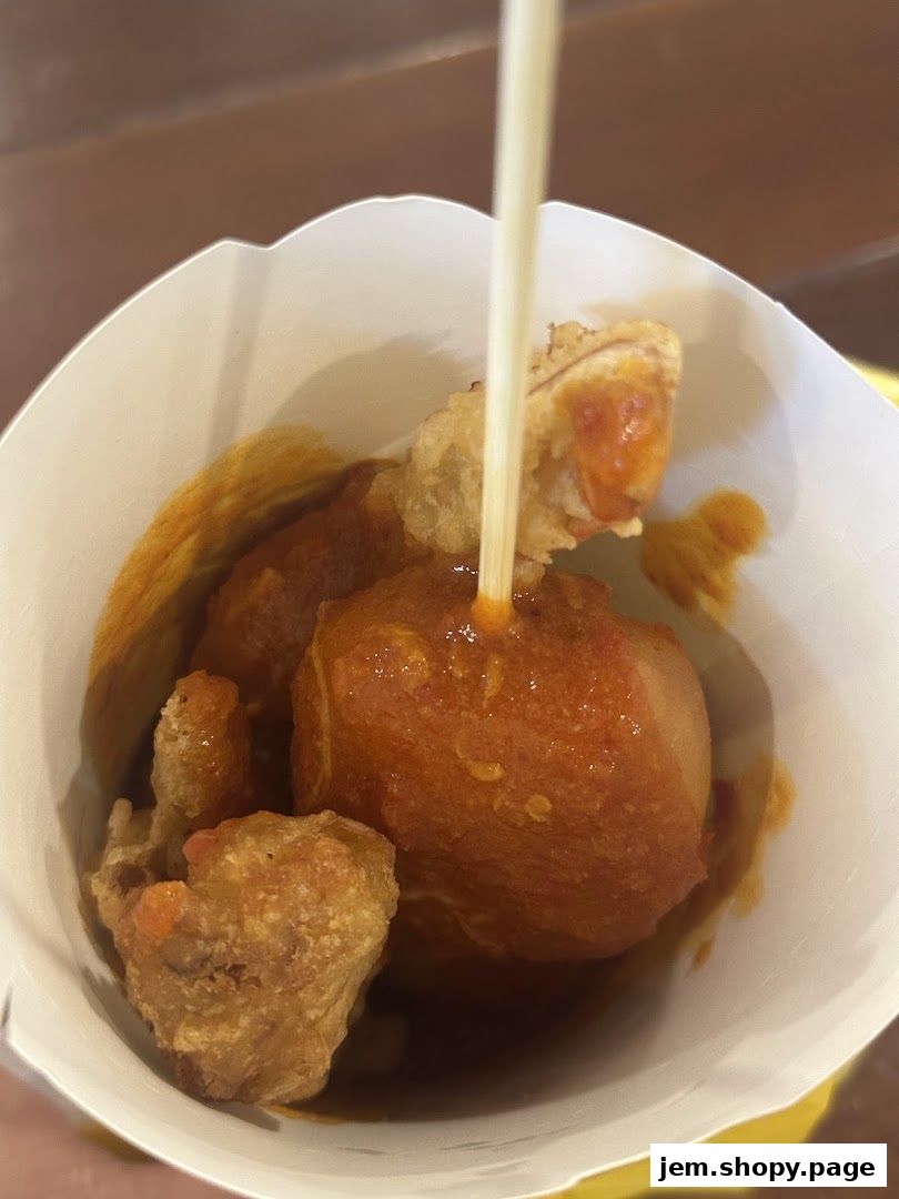 A close-up of Old Chang Kee's signature curry puff and other fried snacks in a paper container.