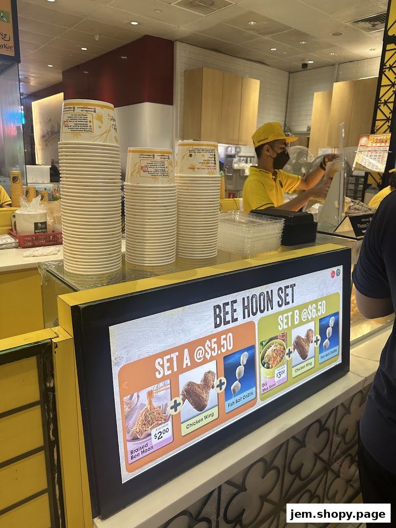 A digital menu board displays Bee Hoon sets with prices and images of food items.
