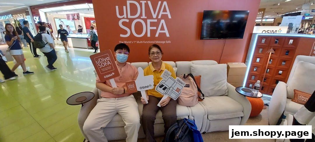 Two people sit on a massage sofa, holding promotional signs for OSIM uDiva Sofa.