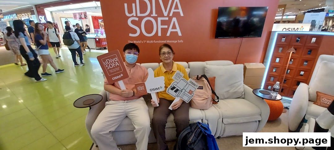 Two people sit on a massage sofa, holding promotional signs for OSIM uDiva Sofa.