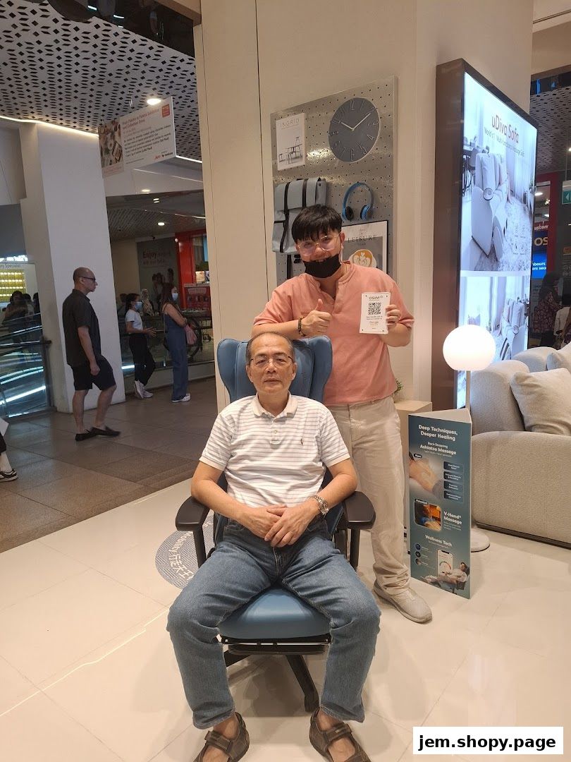 A man sits in a massage chair while another man stands behind him holding a QR code.