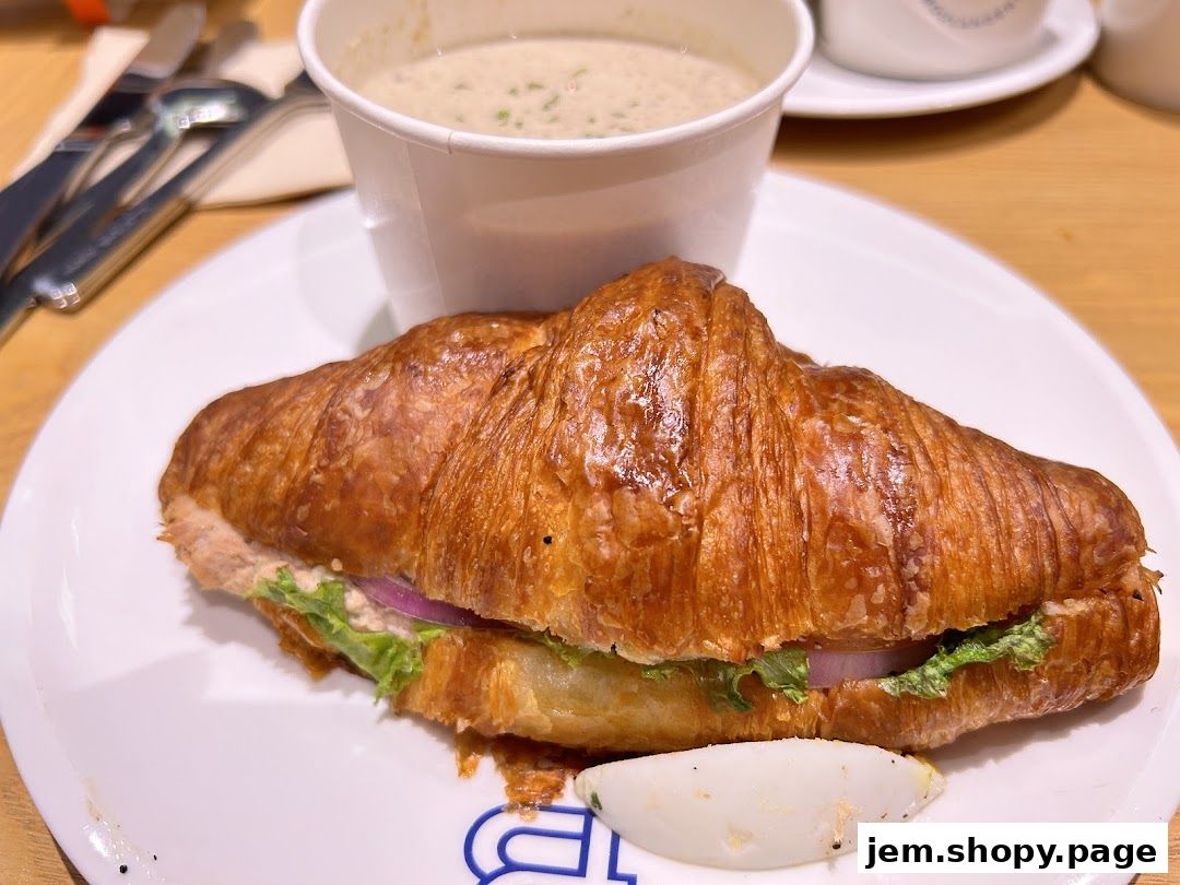 A croissant sandwich with soup and cutlery on a white plate.