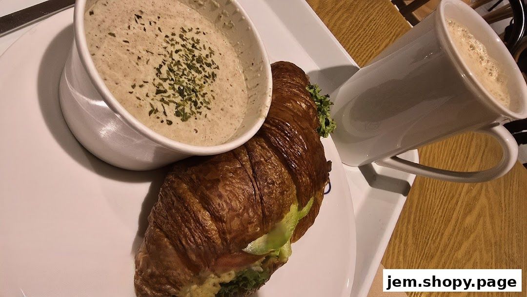 A croissant sandwich with soup and a coffee mug on a white tray.