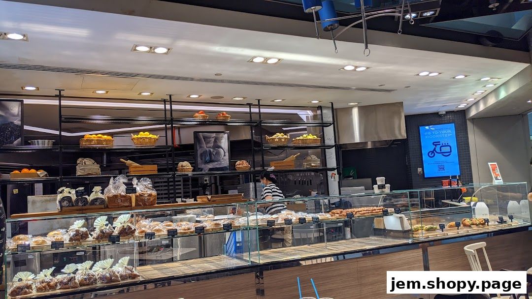 A bakery display case filled with various breads and pastries, with a staff member behind the counter.