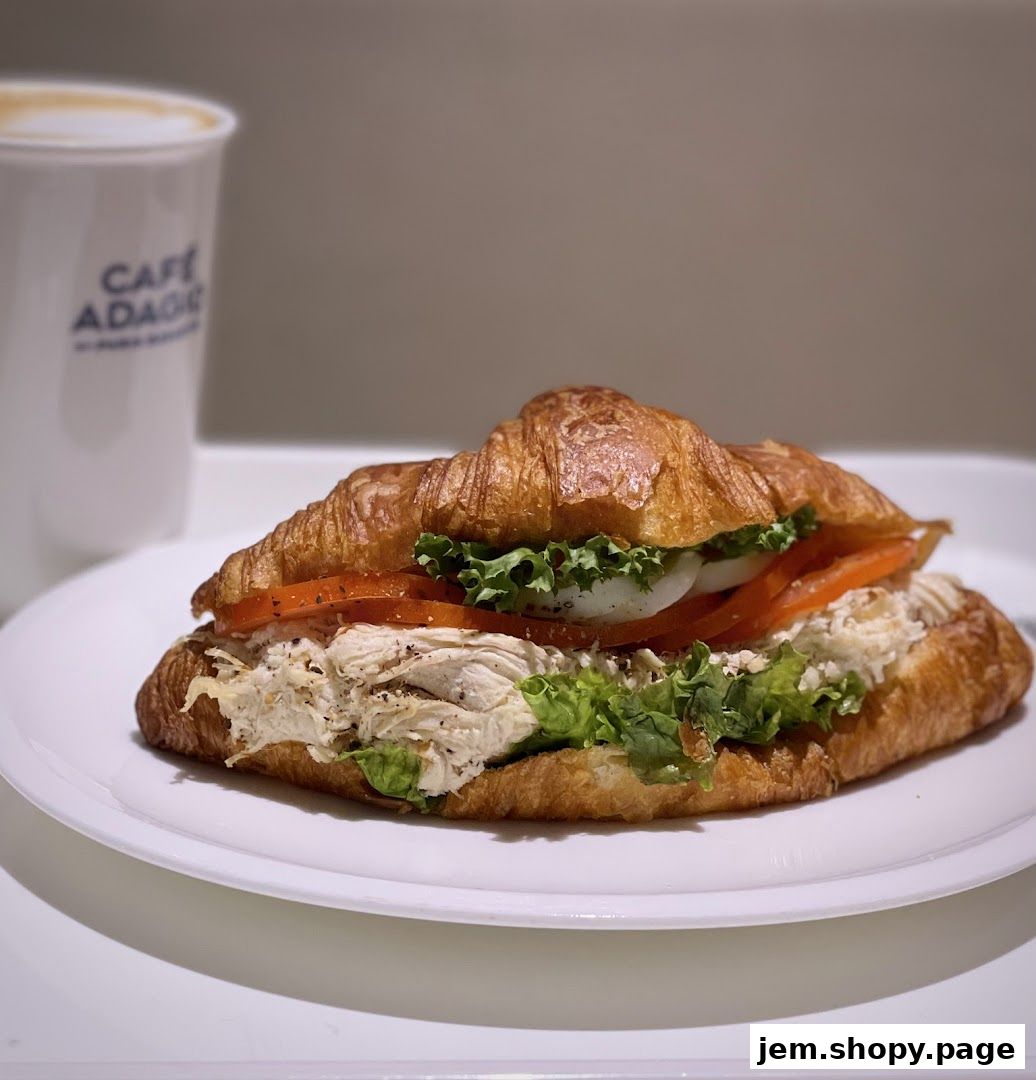 A delicious chicken salad croissant sandwich with lettuce, tomato, and onion, served with a coffee.