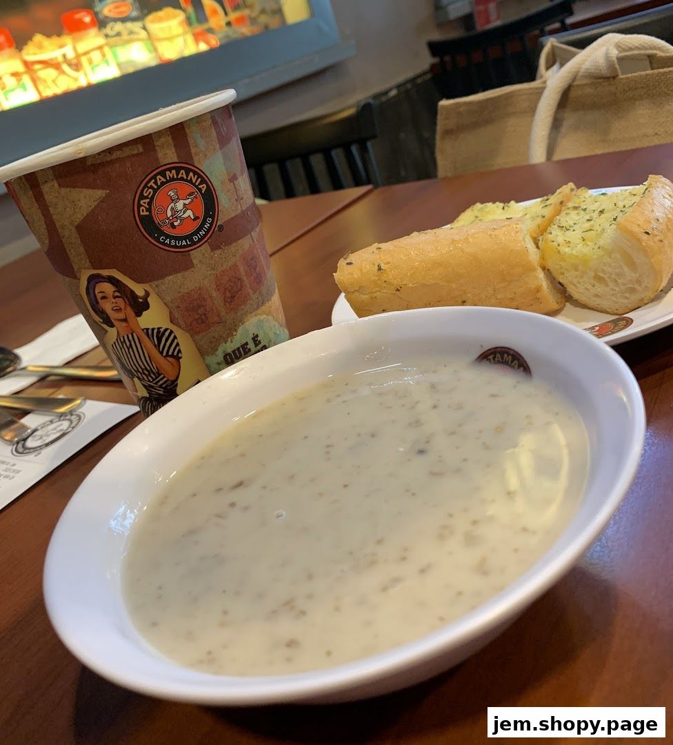 A bowl of creamy soup and garlic bread served with a PastaMania branded cup.