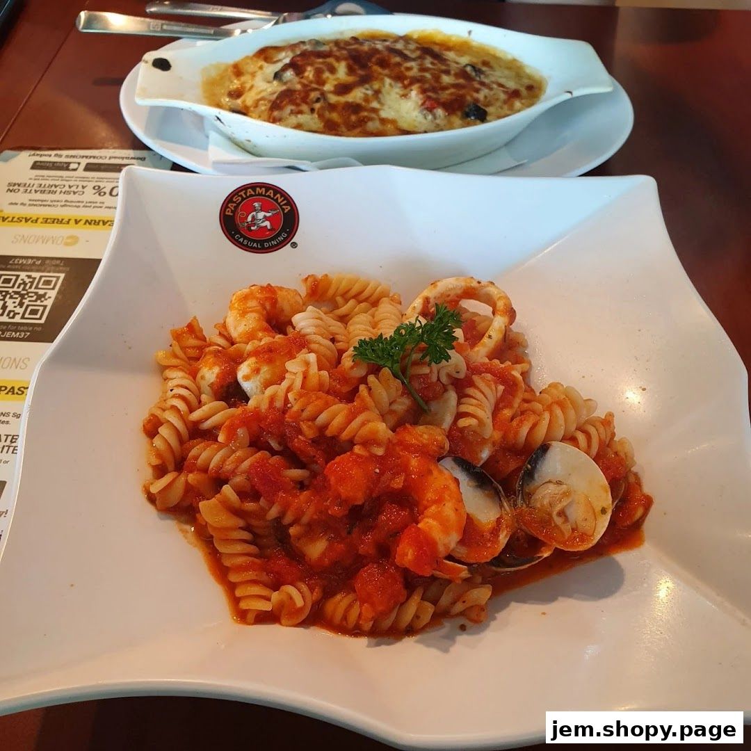 A plate of seafood pasta with tomato sauce and a baked dish in the background.