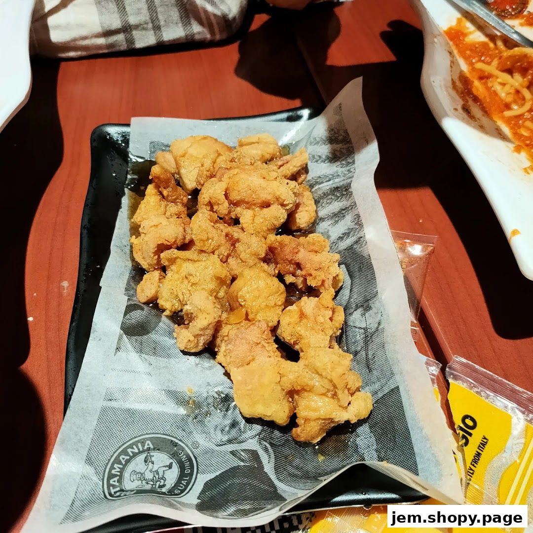 A plate of crispy fried chicken bites served on a black platter with branded paper.
