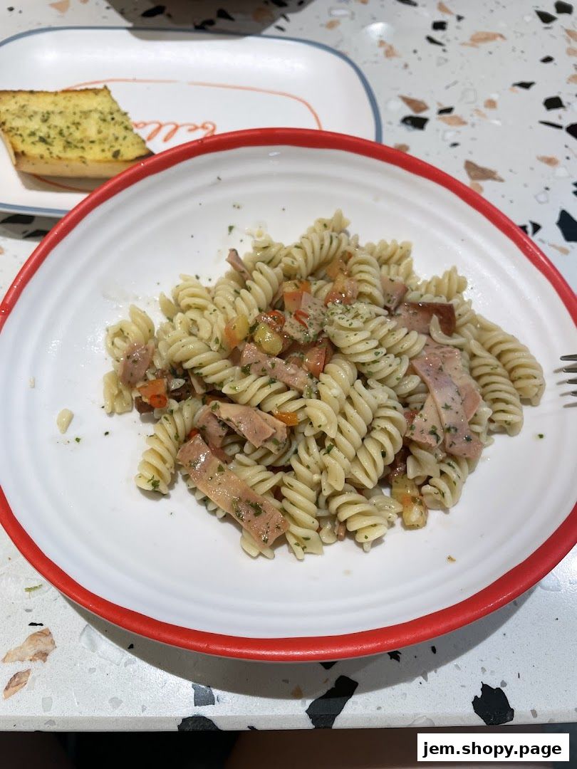 A plate of fusilli pasta with ham and tomatoes, served with garlic bread.