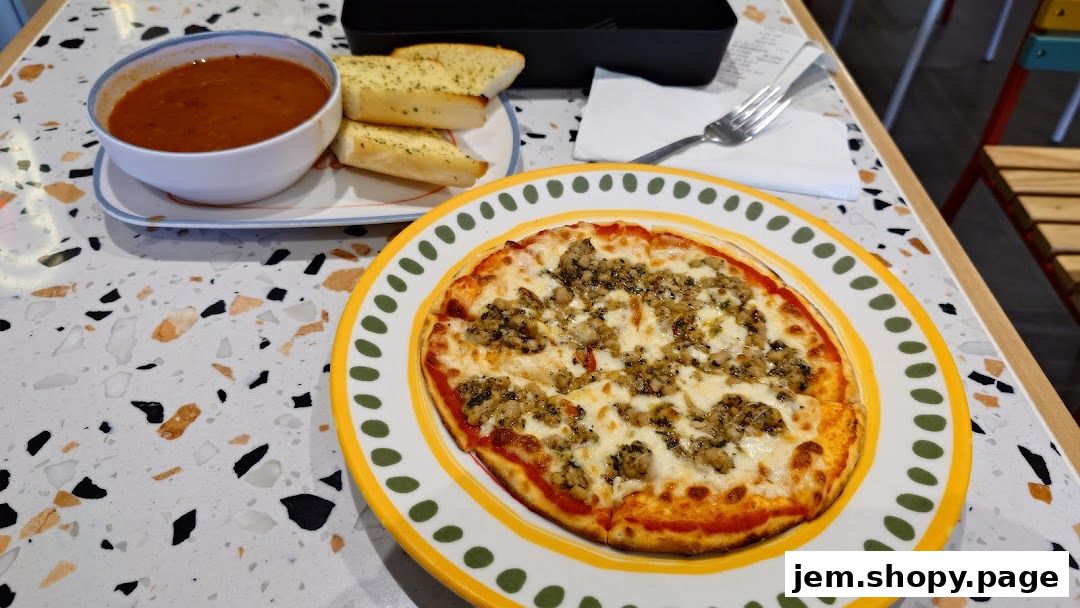 A delicious mini pizza with soup and garlic bread served on a terrazzo table.